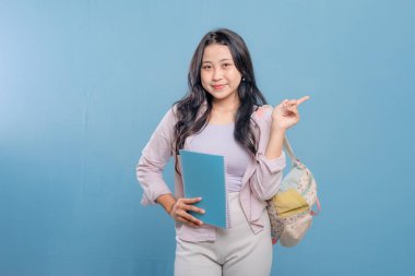 Bir kadın elinde mavi bir kitap tutuyor ve önemli bir şeye işaret ediyor. Gülümsüyor ve mutlu.