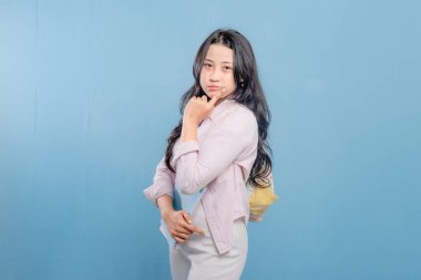 Bir kadın elinde mavi bir kitap ve pembe bir kitap tutuyor. Kameraya bakıyor ve düşünüyor.