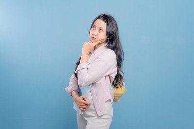 Bir kadın elinde mavi bir kitap ve pembe bir kitap tutuyor. Kameraya bakıyor ve düşünüyor.