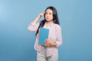 Bir kadın elinde mavi bir kitap ve pembe bir kitap tutuyor. Kameraya bakıyor ve düşünüyor.