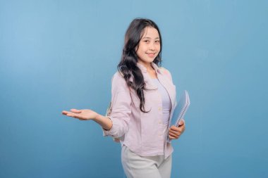 Bir kadın elinde mavi bir kitap tutuyor ve önemli bir şeye işaret ediyor. Gülümsüyor ve mutlu.