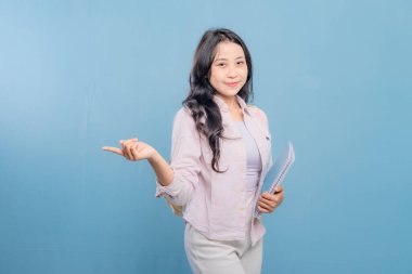 Bir kadın elinde mavi bir kitap tutuyor ve önemli bir şeye işaret ediyor. Gülümsüyor ve mutlu.