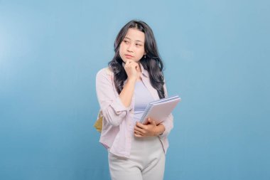 Bir kadın elinde mavi bir kitap ve pembe bir kitap tutuyor. Kameraya bakıyor ve düşünüyor.