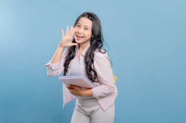 Bir kadın elinde bir yığın kitap tutarken gülümsüyor ve kameraya el sallıyor. Mutluluk ve heyecan kavramı, kadının kitaplarıyla gurur duyması ya da bilgisini başkalarıyla paylaşmaya istekli olması gibi.