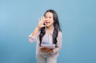 Bir kadın elinde bir yığın kitap tutarken gülümsüyor ve kameraya el sallıyor. Mutluluk ve heyecan kavramı, kadının kitaplarıyla gurur duyması ya da bilgisini başkalarıyla paylaşmaya istekli olması gibi.