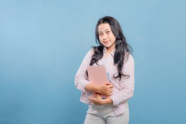 Bir kadın bir kitap ve bir sırt çantası tutuyor. Gülümsüyor ve kameraya bakıyor. Kendine güven ve hazır olma kavramı, çünkü kadın önümüzdeki güne hazır.