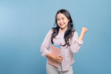 Bir kadın bir kitap ve bir sırt çantası tutuyor. Gülümsüyor ve kameraya bakıyor. Kendine güven ve hazır olma kavramı, çünkü kadın önümüzdeki güne hazır.