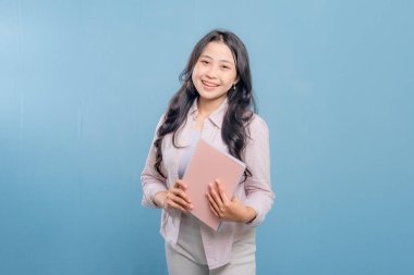 Bir kadın bir kitap ve bir sırt çantası tutuyor. Gülümsüyor ve kameraya bakıyor. Kendine güven ve hazır olma kavramı, çünkü kadın önümüzdeki güne hazır.