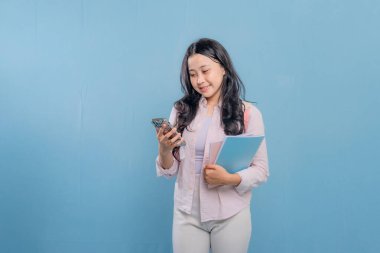 Bir kadın elinde cep telefonu ve bir yığın kitap tutuyor. Gülümsüyor ve mutlu.