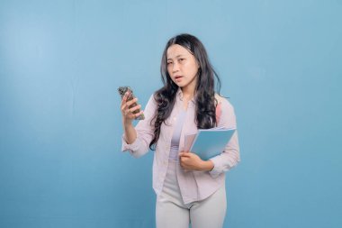 Bir kadın elinde cep telefonu ve bir yığın kitap tutuyor. Gülümsüyor ve mutlu.