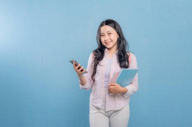 Bir kadın elinde cep telefonu ve bir yığın kitap tutuyor. Gülümsüyor ve mutlu.