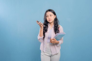 Bir kadın elinde cep telefonu ve bir yığın kitap tutuyor. Gülümsüyor ve mutlu.