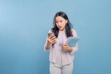 Bir kadın elinde cep telefonu ve bir yığın kitap tutuyor. O, yüzünde şaşırmış bir ifadeyle telefona bakıyor.