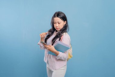 Bir kadın elinde cep telefonu ve bir yığın kitap tutuyor. Gülümsüyor ve mutlu.