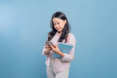 Bir kadın elinde cep telefonu ve bir yığın kitap tutuyor. Gülümsüyor ve mutlu.