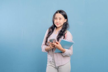 Bir kadın elinde cep telefonu ve bir yığın kitap tutuyor. Gülümsüyor ve mutlu.