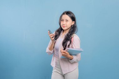 Bir kadın elinde cep telefonu ve bir yığın kitap tutuyor. Gülümsüyor ve mutlu.