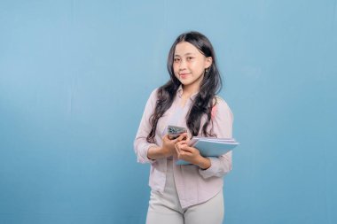 Bir kadın elinde cep telefonu ve bir yığın kitap tutuyor. Gülümsüyor ve mutlu.