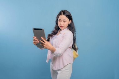 Genç bir kadın elinde bir tablet tutuyor ve gökyüzünü işaret ediyor. Gülümsüyor ve bir şey hakkında heyecanlı ya da meraklı.