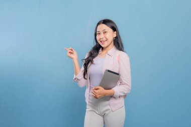 Bir kadın elinde dizüstü bilgisayar ve tablet tutuyor. Gülümsüyor ve kameraya bakıyor.