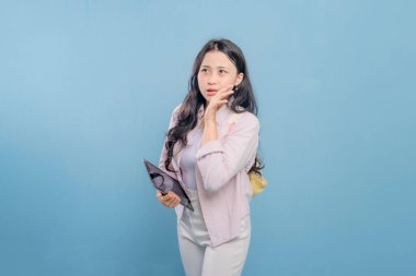 Bir kadın elinde bir tablet tutuyor ve yüksek sesle gürültü yapıyor. Pembe gömlek ve beyaz pantolon giyiyor.