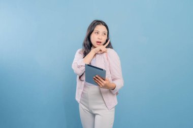 Bir kadın elinde bir tablet tutuyor ve bir şeyi işaret ediyor. Pembe gömlek ve beyaz pantolon giyiyor.