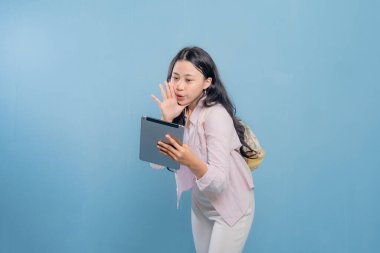 Bir kadın elinde bir tablet tutuyor ve yüksek sesle gürültü yapıyor. Pembe gömlek ve beyaz pantolon giyiyor.