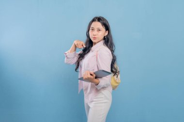 Bir kadın elinde bir tablet tutuyor ve bir şeyi işaret ediyor. Pembe gömlek ve beyaz pantolon giyiyor.