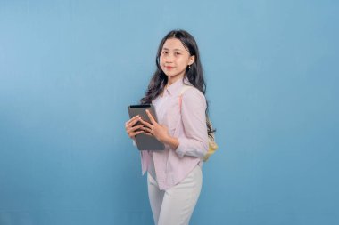 Bir kadın elinde dizüstü bilgisayar ve tablet tutuyor. Gülümsüyor ve kameraya bakıyor.