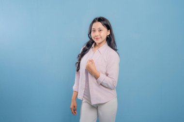 Pembe gömlekli ve beyaz pantolonlu bir kadın resim için poz veriyor. Gülümsüyor ve mutlu.