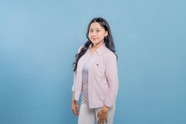 Pembe gömlekli ve beyaz pantolonlu bir kadın resim için poz veriyor. Gülümsüyor ve mutlu.