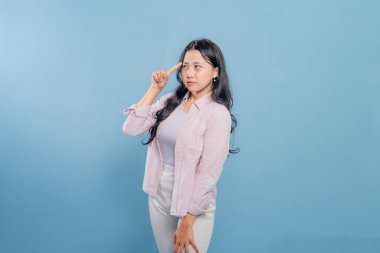 Mavi bir duvarın önünde pembe ceketli ve beyaz pantolonlu bir kadın duruyor. Aşağıya bakıyor ve derin düşüncelere dalmış.