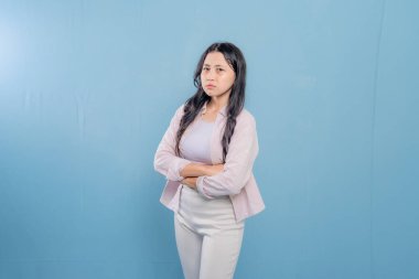 Pembe gömlekli ve beyaz pantolonlu bir kadın kollarını kavuşturmuş duruyor. Mutsuz görünüyor ve kaşlarını çatıyor.