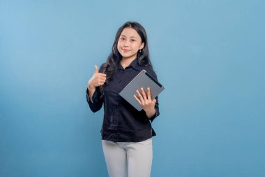 Bir kadın gülümsüyor ve elinde bir tablet tutuyor. O, siyah bir gömlek ve beyaz pantolon giyiyor. Profesyonellik ve güven kavramı