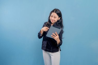 Bir kadın tablet tutuyor ve gülümsüyor. O, siyah bir gömlek ve beyaz pantolon giyiyor. Verimlilik ve odaklanma kavramı, kadının çalışma veya öğrenim için tableti kullanması gibi