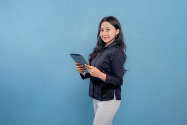 Bir kadın gülümsüyor ve elinde bir tablet tutuyor. O, siyah bir gömlek ve beyaz pantolon giyiyor. Profesyonellik ve güven kavramı