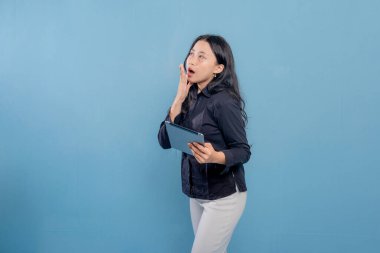 Bir kadın elinde bir tablet tutuyor ve ağzı açık. Şok ya da şaşkınlık içinde.