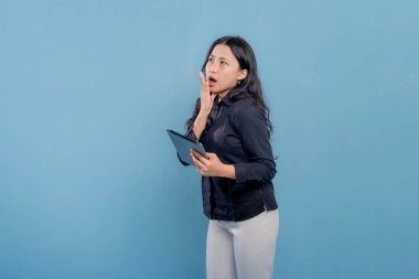 Bir kadın elinde bir tablet tutuyor ve ağzı açık. Şok ya da şaşkınlık içinde.