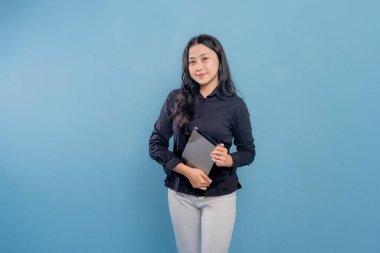 Bir kadın gülümsüyor ve elinde bir tablet tutuyor. O, siyah bir gömlek ve beyaz pantolon giyiyor. Profesyonellik ve güven kavramı