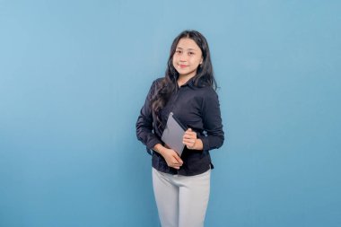 Bir kadın gülümsüyor ve elinde bir tablet tutuyor. O, siyah bir gömlek ve beyaz pantolon giyiyor. Profesyonellik ve güven kavramı