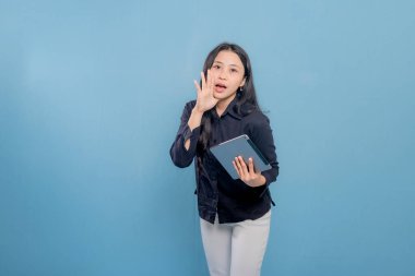 Siyah gömlekli ve beyaz pantolonlu bir kadın elinde bir tablet tutuyor. Kameraya bakıyor ve ciddi ya da odaklanmış bir ruh halinde.