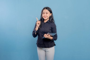 Bir kadın gülümsüyor ve elinde bir tablet tutuyor. O, siyah bir gömlek ve beyaz pantolon giyiyor. Profesyonellik ve güven kavramı