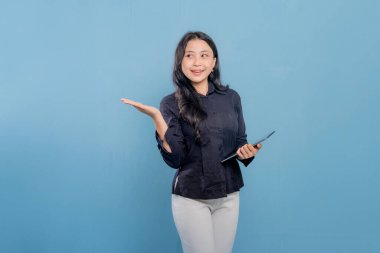 Bir kadın gülümsüyor ve elinde bir tablet tutuyor. O, siyah bir gömlek ve beyaz pantolon giyiyor. Profesyonellik ve güven kavramı