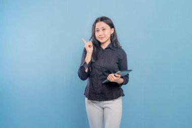 Bir kadın gülümsüyor ve elinde bir tablet tutuyor. O, siyah bir gömlek ve beyaz pantolon giyiyor. Profesyonellik ve güven kavramı