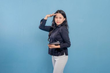 Siyah gömlek ve beyaz pantolon giyen bir kadın elinde bir tablet tutuyor. Yukarı bakıyor ve gökyüzünü işaret ediyor.