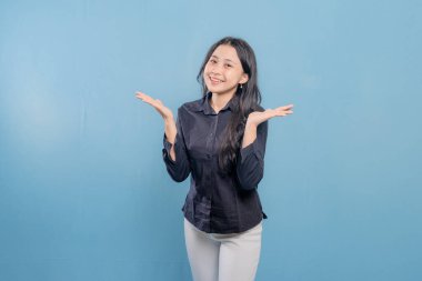 Bir kadın gülümsüyor ve ellerini havaya kaldırıyor. Siyah gömlek ve beyaz pantolon giyiyor.