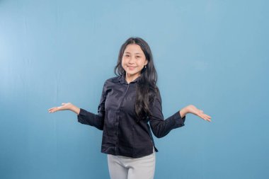 Bir kadın gülümsüyor ve ellerini havaya kaldırıyor. Siyah gömlek ve beyaz pantolon giyiyor.