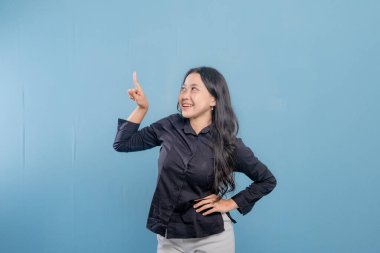 Bir kadın parmağıyla bir şeyi işaret ediyor. O, siyah bir gömlek ve beyaz pantolon giyiyor. Gülümsüyor ve mutlu.