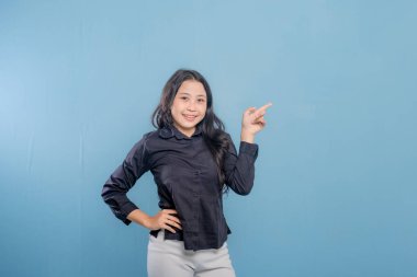 Bir kadın parmağıyla bir şeyi işaret ediyor. O, siyah bir gömlek ve beyaz pantolon giyiyor. Gülümsüyor ve mutlu.