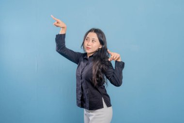 Bir kadın parmağıyla bir şeyi işaret ediyor. O, siyah bir gömlek ve beyaz pantolon giyiyor. Gülümsüyor ve mutlu.